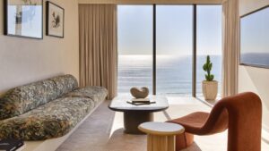 A stylish interior of a living room with a beach view, featuring a floral sofa, modern furniture, and large windows allo
